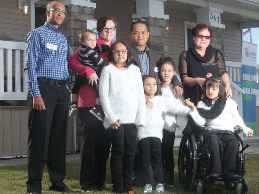 Gezai Gebrekidan, left, and the Dumlao family, from left, mom Suzanne holding Jacob, Zoe, dad Jeffrey, Finley, Carmella and Autumn, along with grandmother Lili Desjardins, all pose in front of their new homes during a double dedication ceremony by Habitat for Humanity for families with special needs children in the Redstone neighbourhood Wednesday November 9, 2016. Ted Rhodes Photo Postmedia Calgary